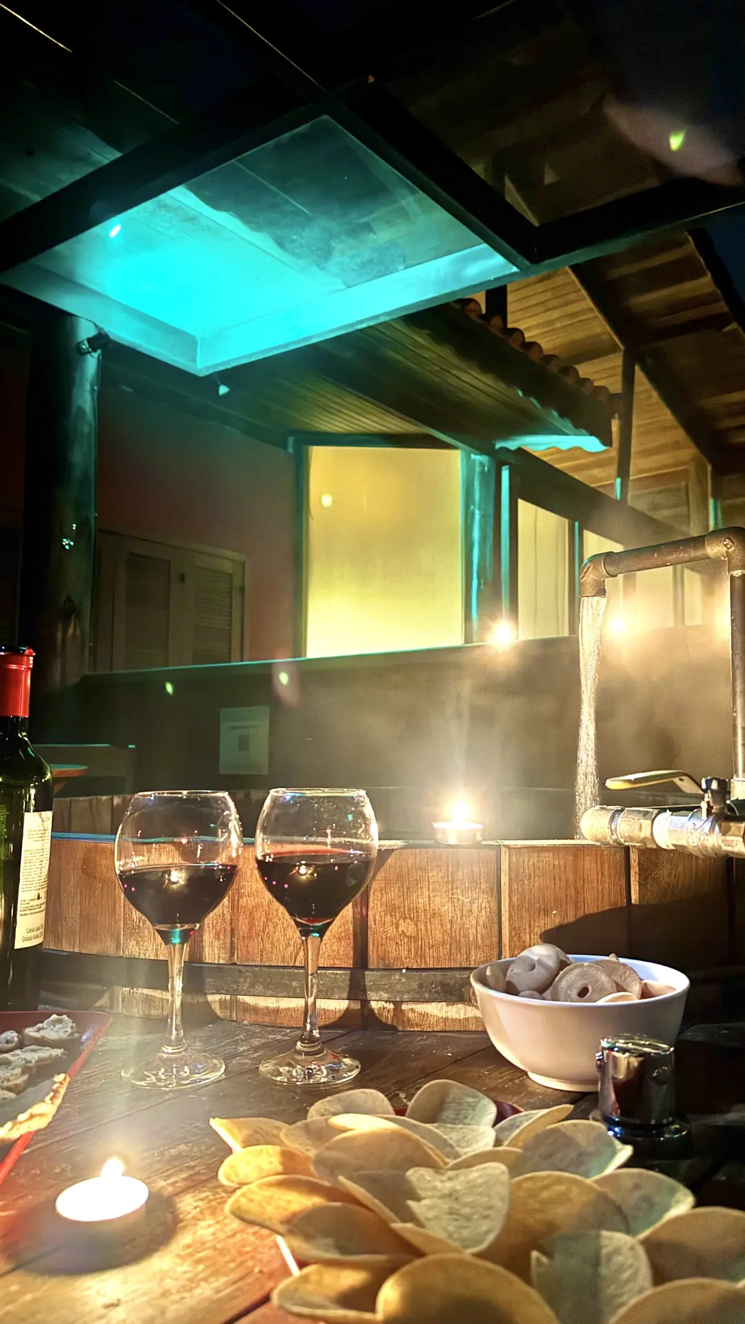 Ofurô aquecido à noite sob luz azul-turquesa, com a mesa posta em primeiro plano